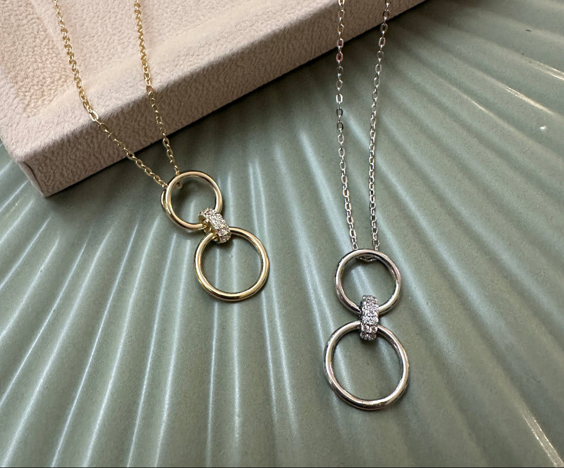 Two necklaces with interlocking rings  with a sparkly link on a textured surface