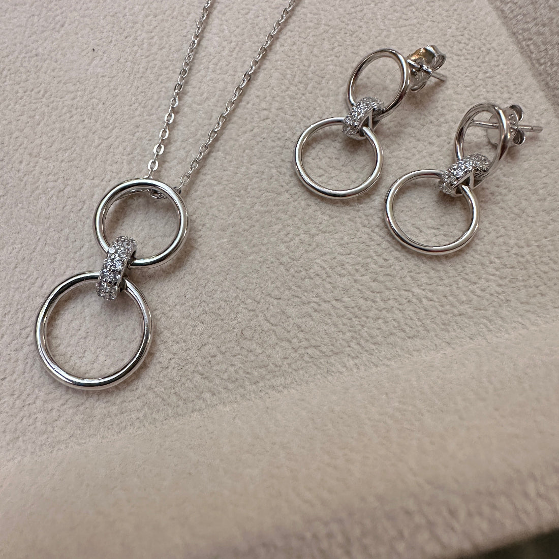 Silver jewellery set with 2 rings interlocked by a sparkly link on a beige surface