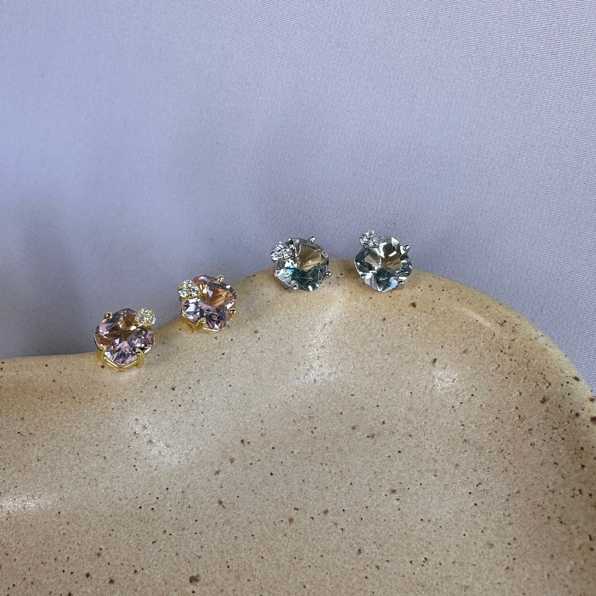 Set of four sterling silver stud earrings set with amethyst gemstones on a textured stone surface with a light gray background