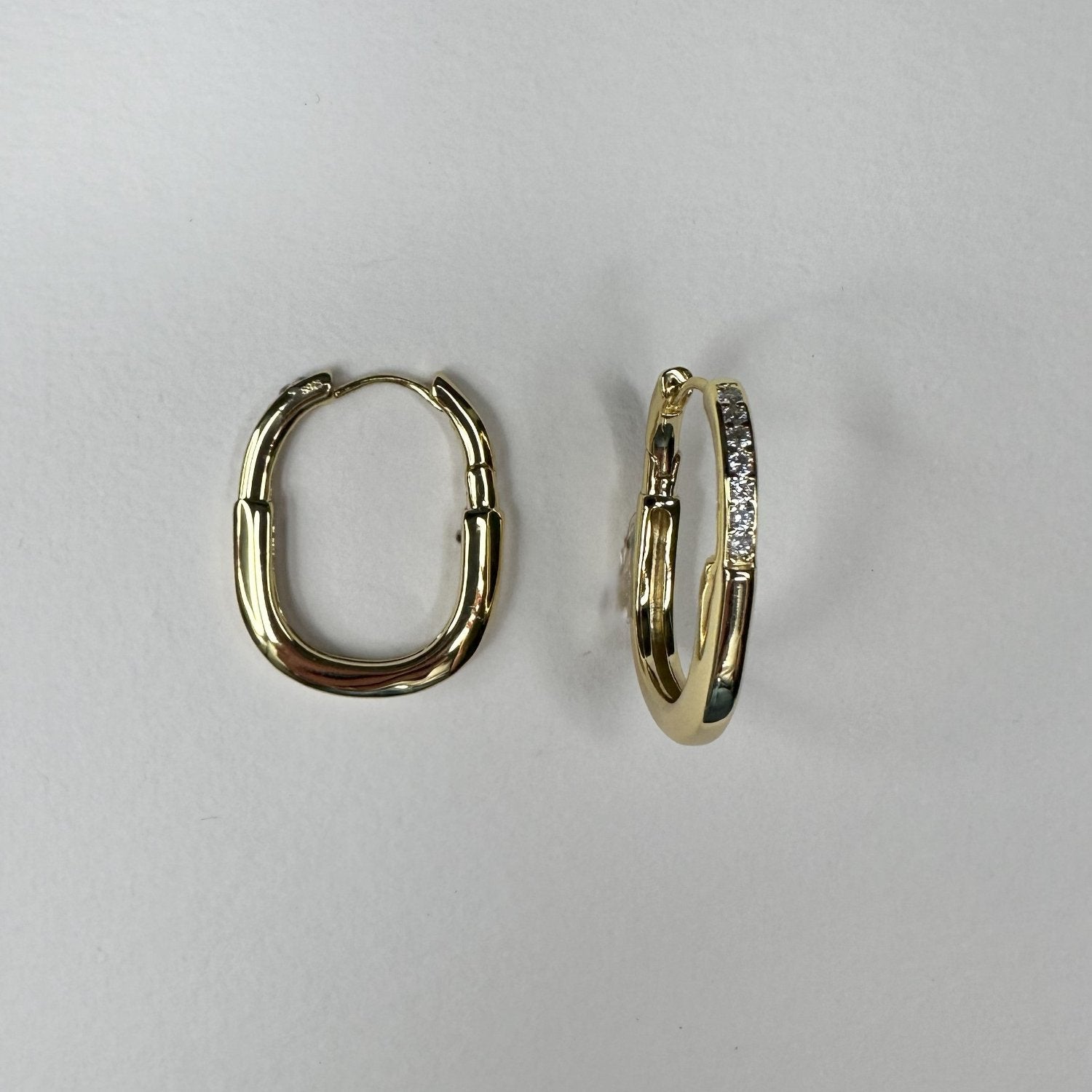 gold oval hoop earrings with gemstones on a white matte plate
