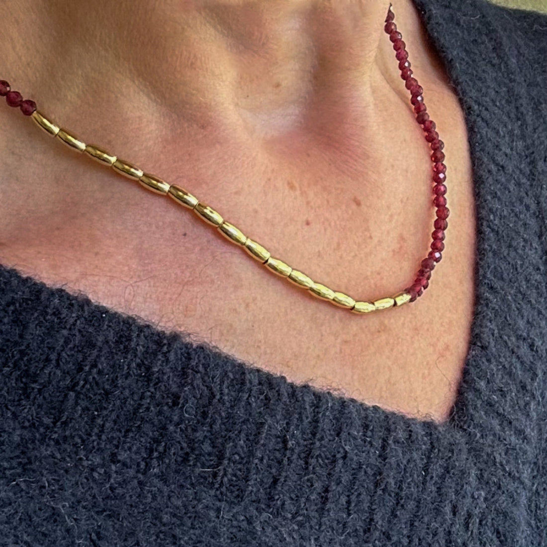 Gold and Ruby coloured bead necklace worn on model with blue jumper