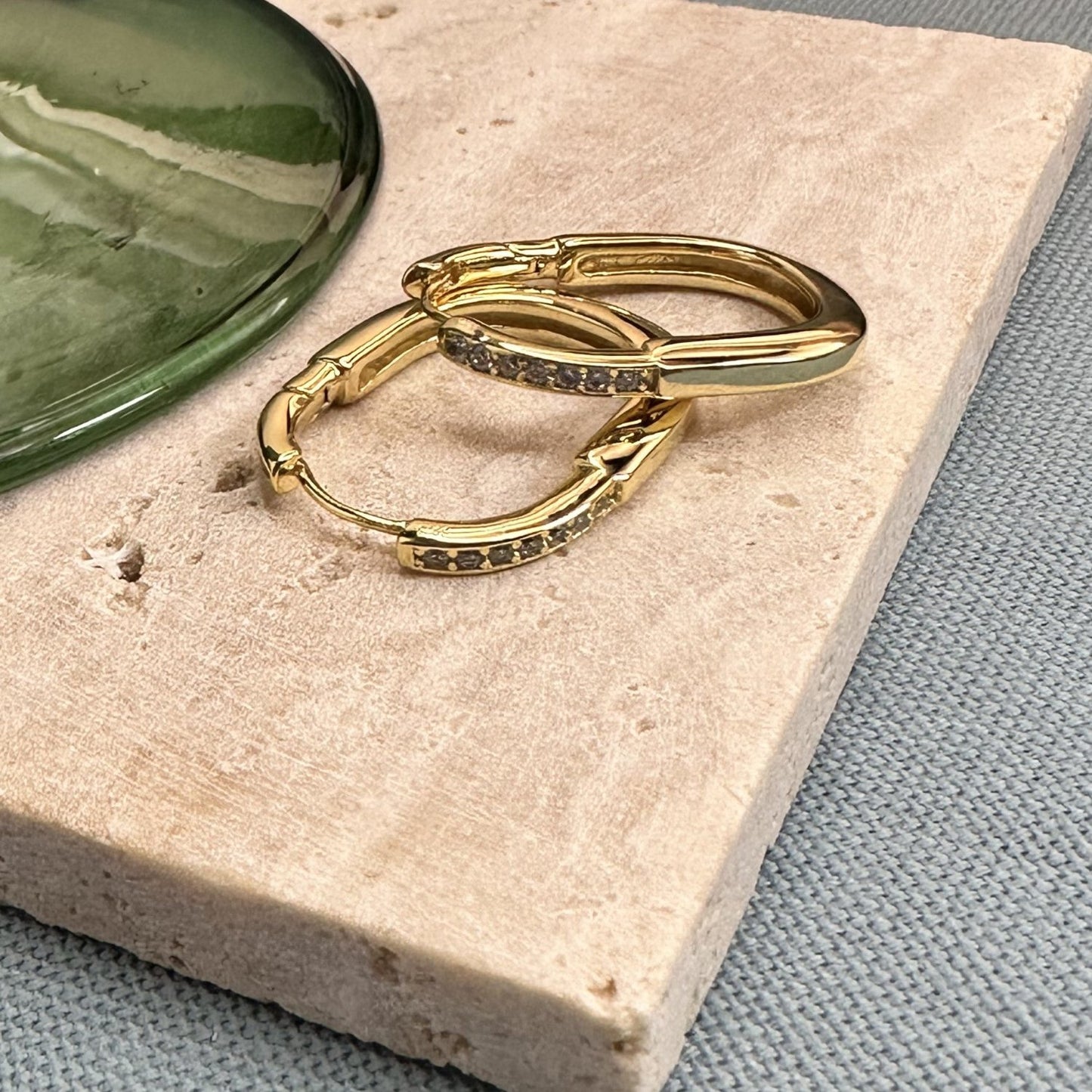 gold oval hoop earrings with gemstones on a wooden surface.