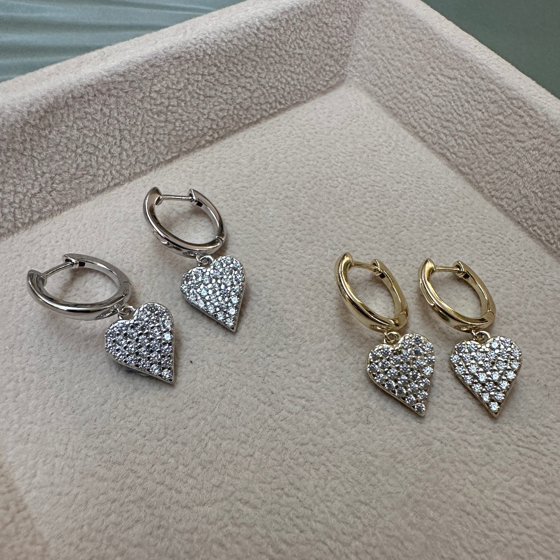 Heart-shaped sparkle charm earrings in silver and gold on a textured surface