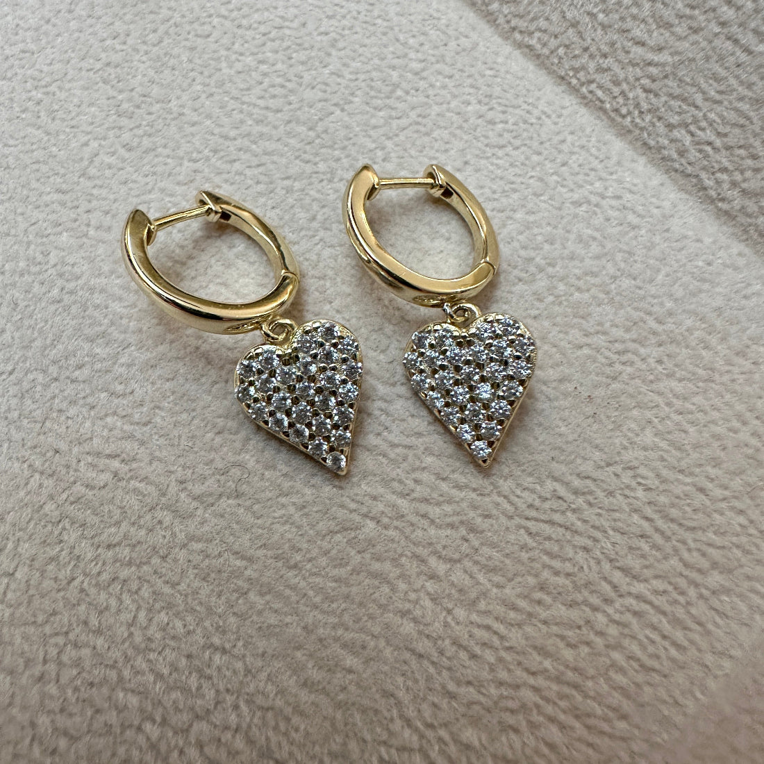 Gold hoop earrings with heart-shaped diamond pendants on a light gray surface