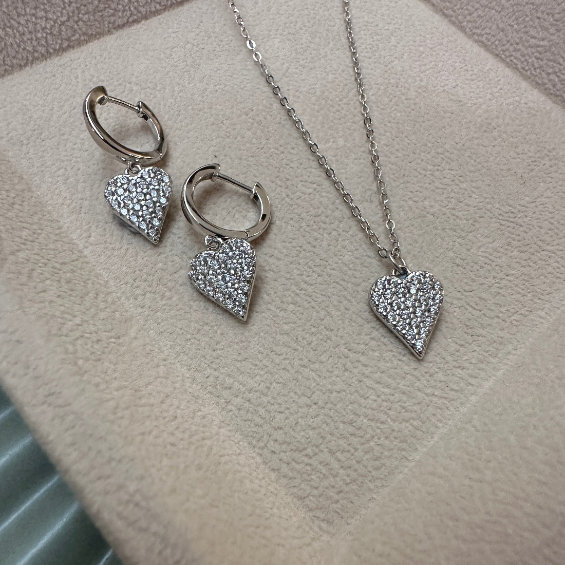 Silver heart-shaped sparkle jewellery set with earrings and a necklace on a textured surface.