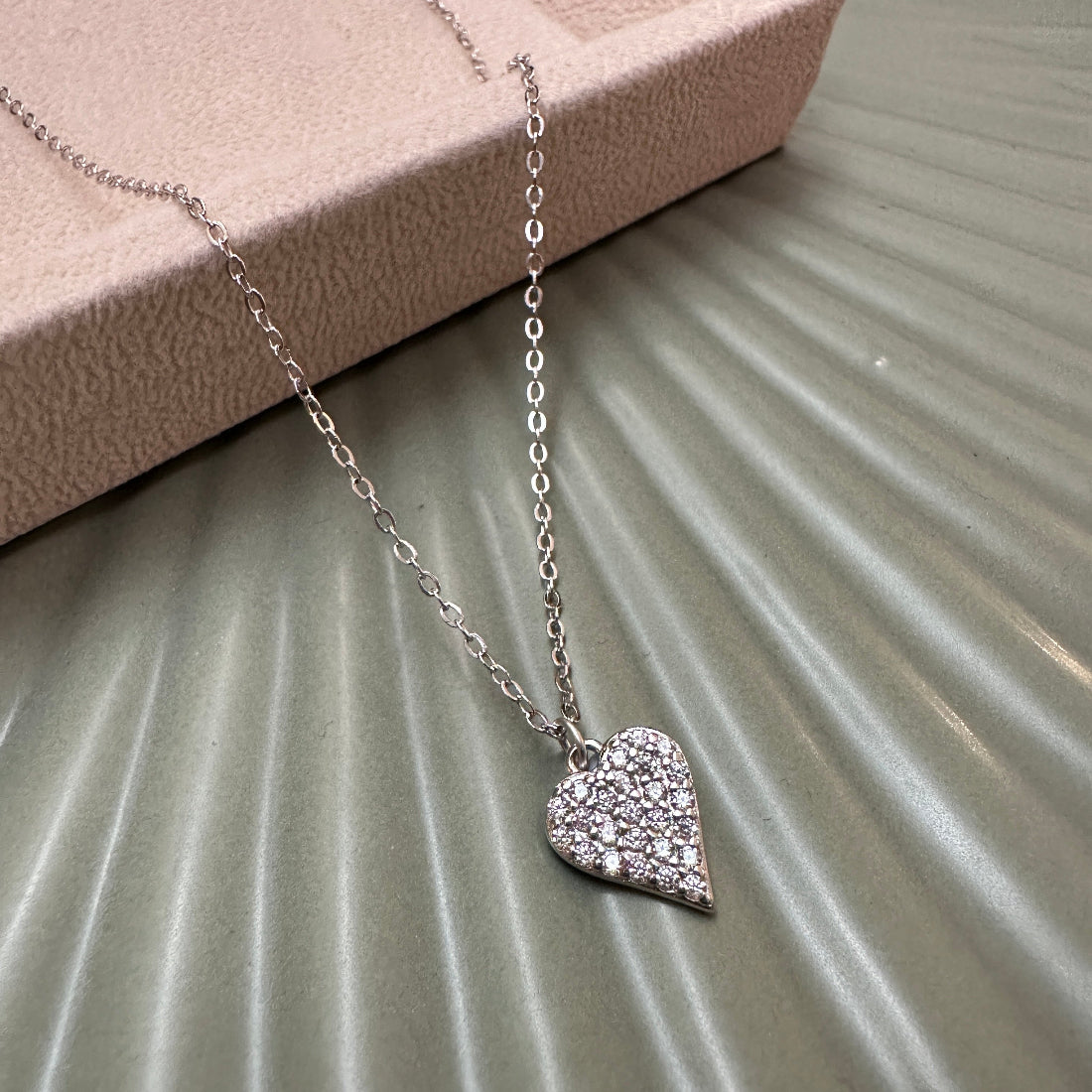Silver heart-shaped sparkly pendant necklace on a textured surface