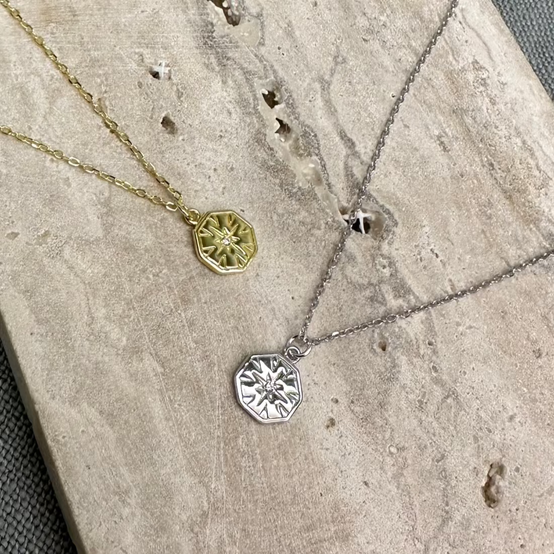 Two Hexagon Charm Pendant Necklaces laid out on a textured surface, one in gold and the other in silver color, showcasing the geometric hexagon charm.