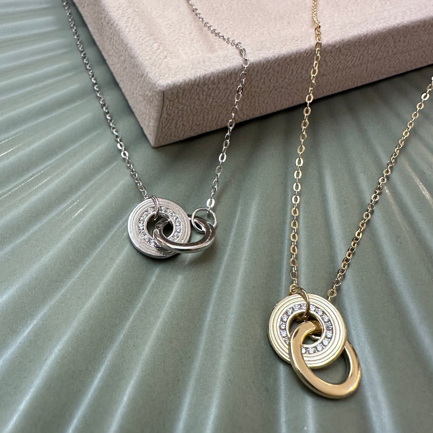 Two necklaces with interlocking circular pendants on a textured surface.