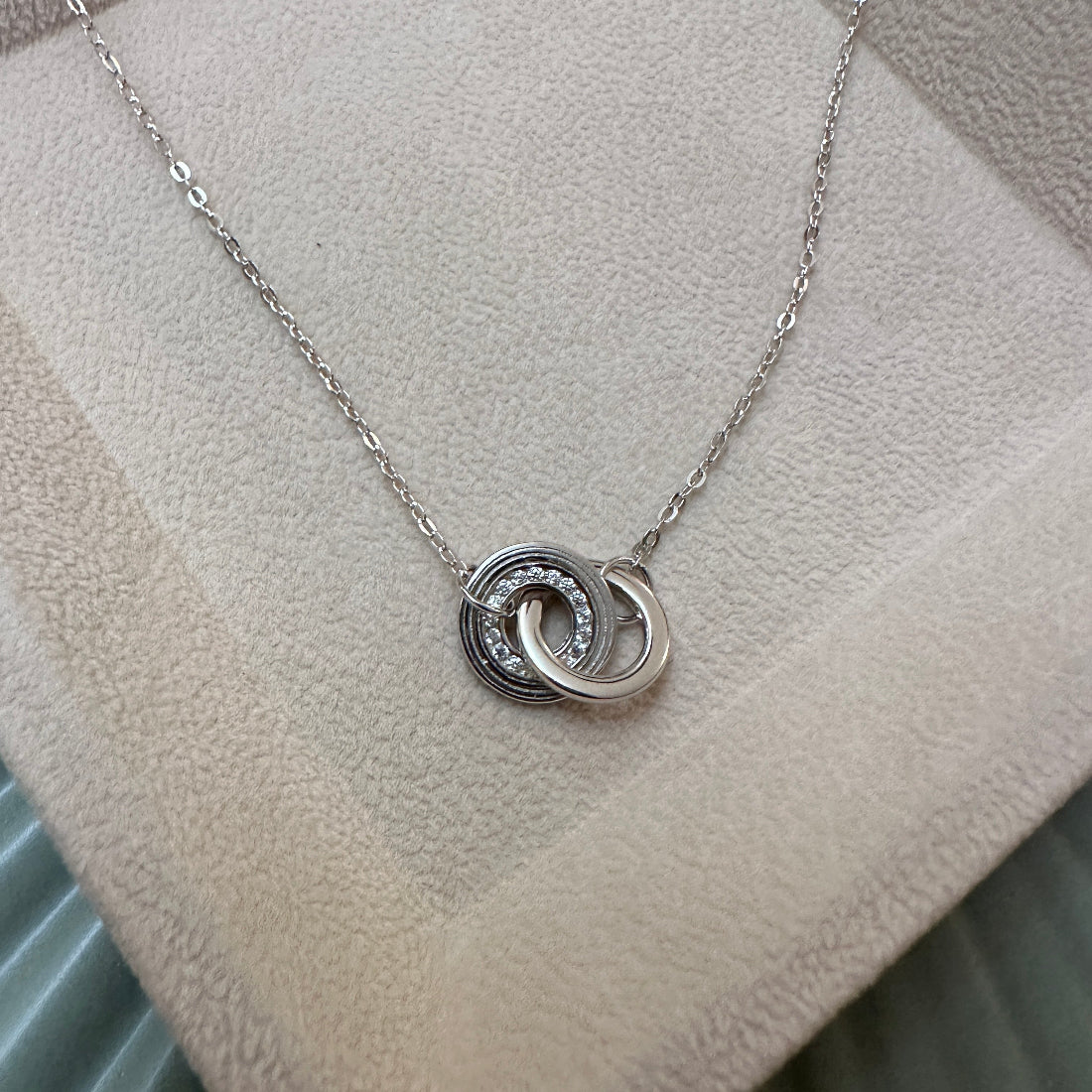 Silver necklace with interlocking rings on a textured surface
