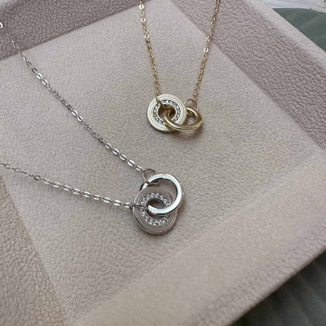 Two silver necklaces with interlocking ring pendants on a textured surface.