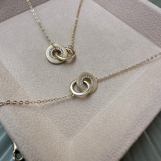 Gold necklaces with interlocking circular pendants on a textured surface