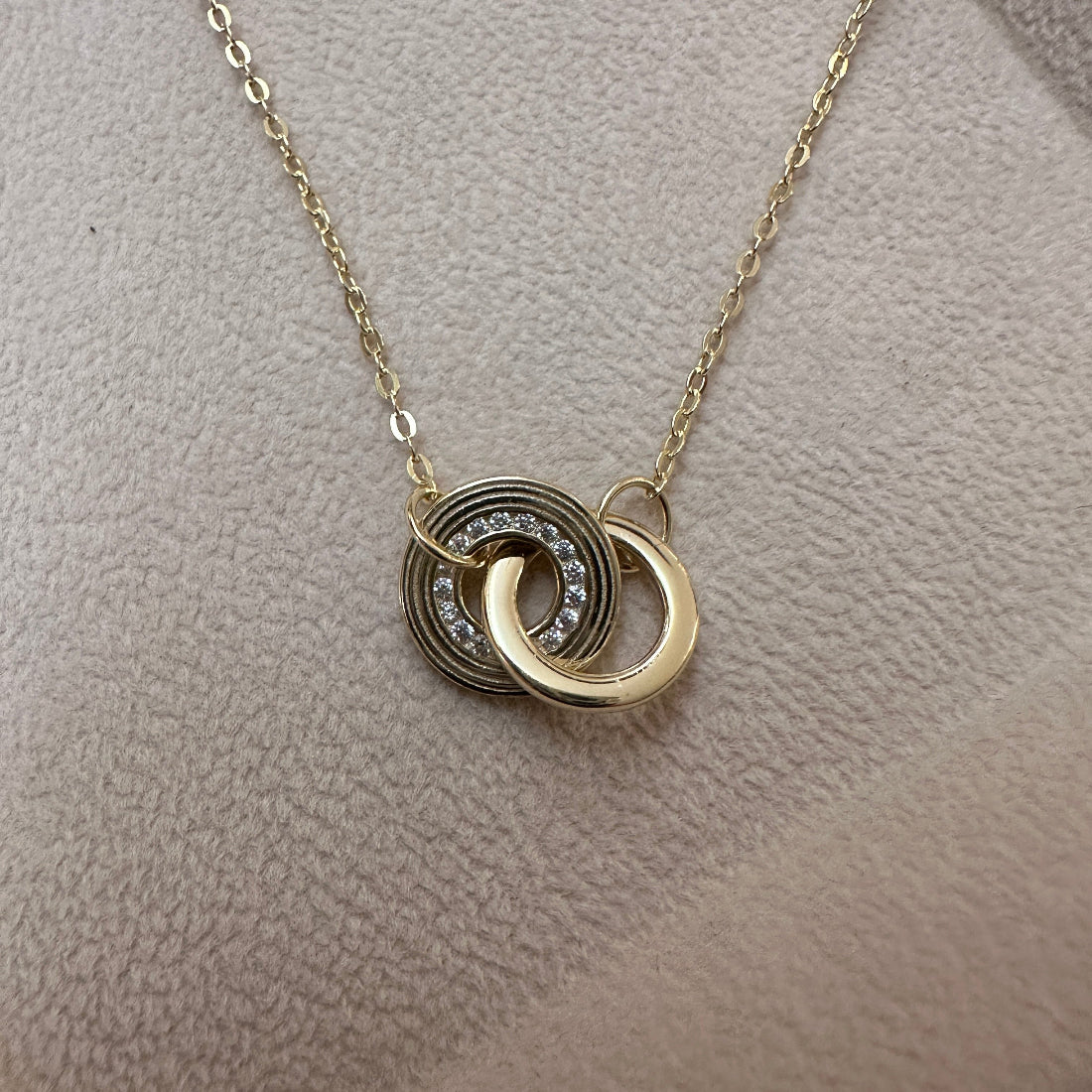 Gold necklace with interlocking rings on a beige fabric background