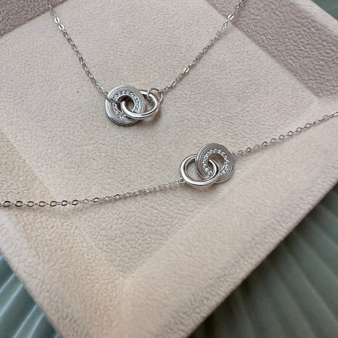 Silver necklace with interlocking rings on a soft fabric background