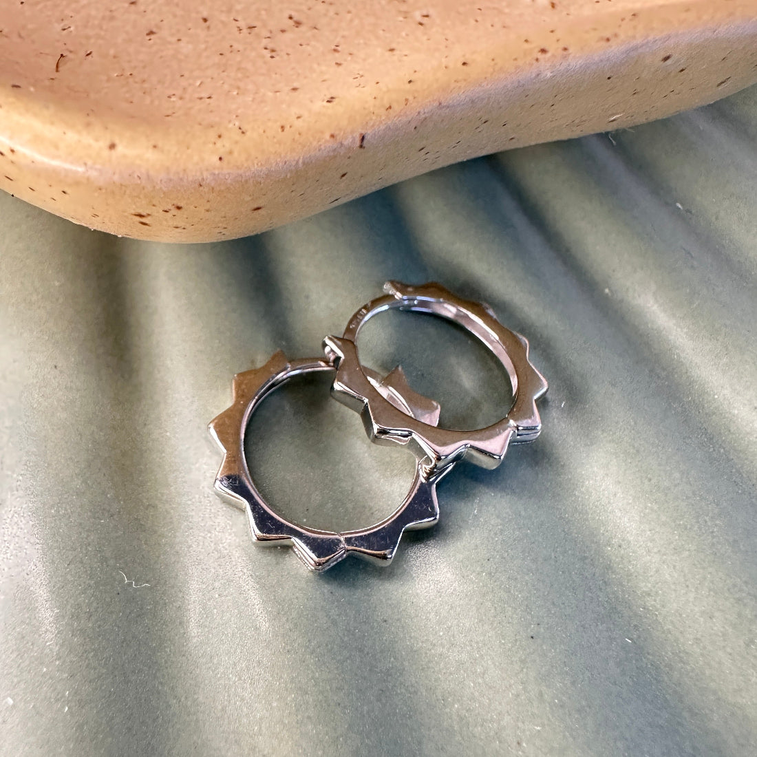 Contemporary sterling silver hoop earrings with jagged edge detail on a textured surface