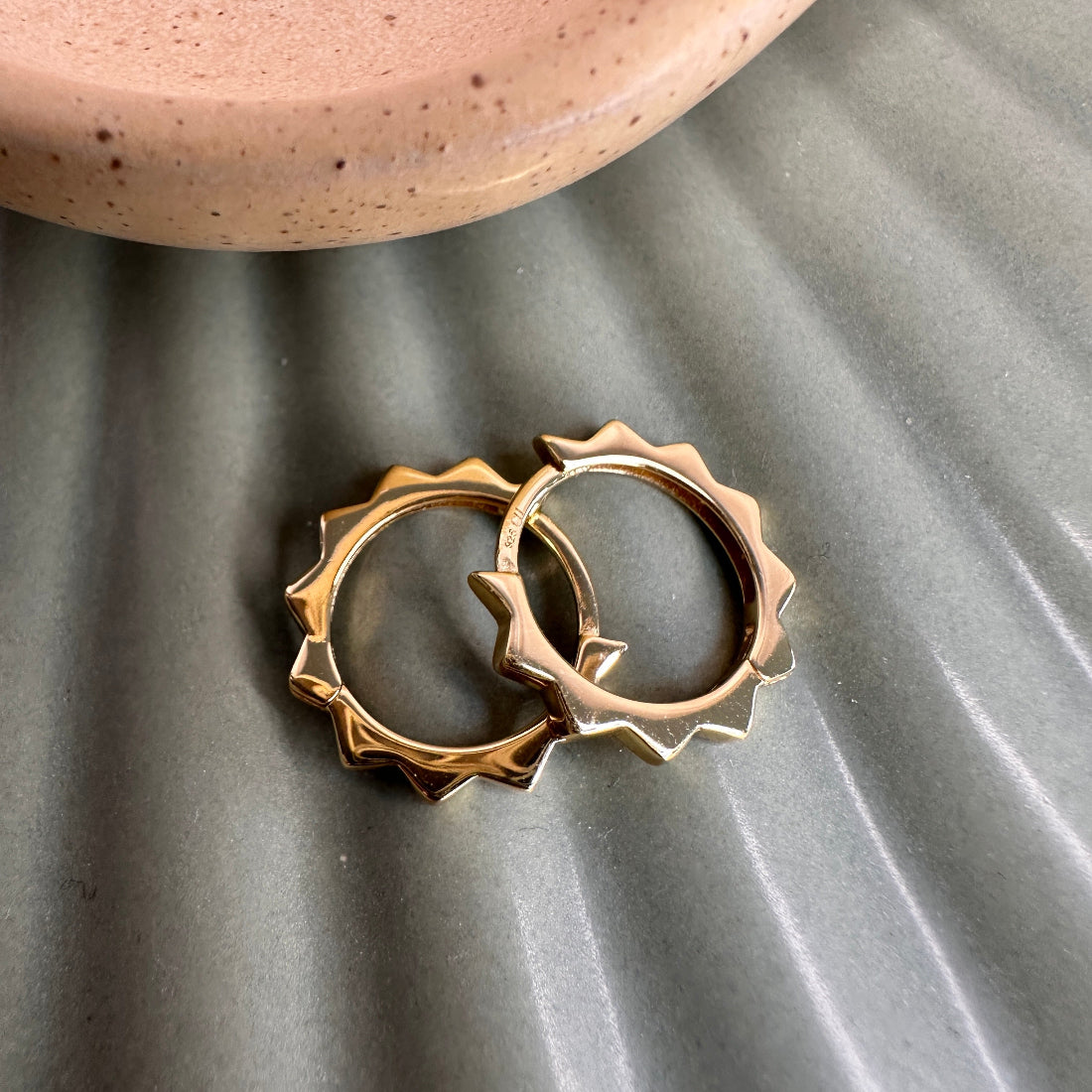 Edgy spike triangular detailed Gold hoop earrings on a textured gray surface with a ceramic dish in the background