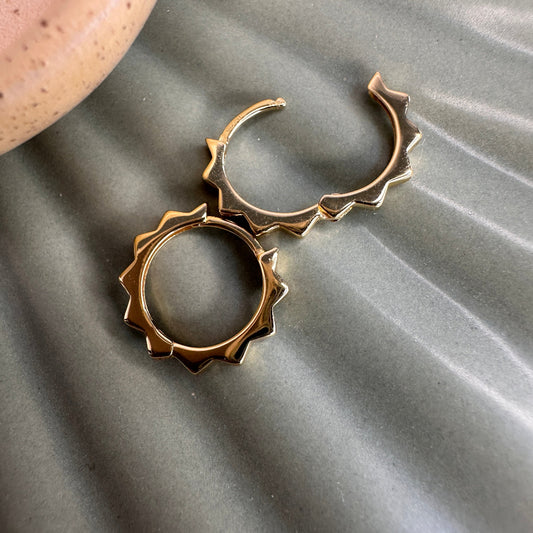 Gold hoop earrings with triangular spike detail on a textured grey surface