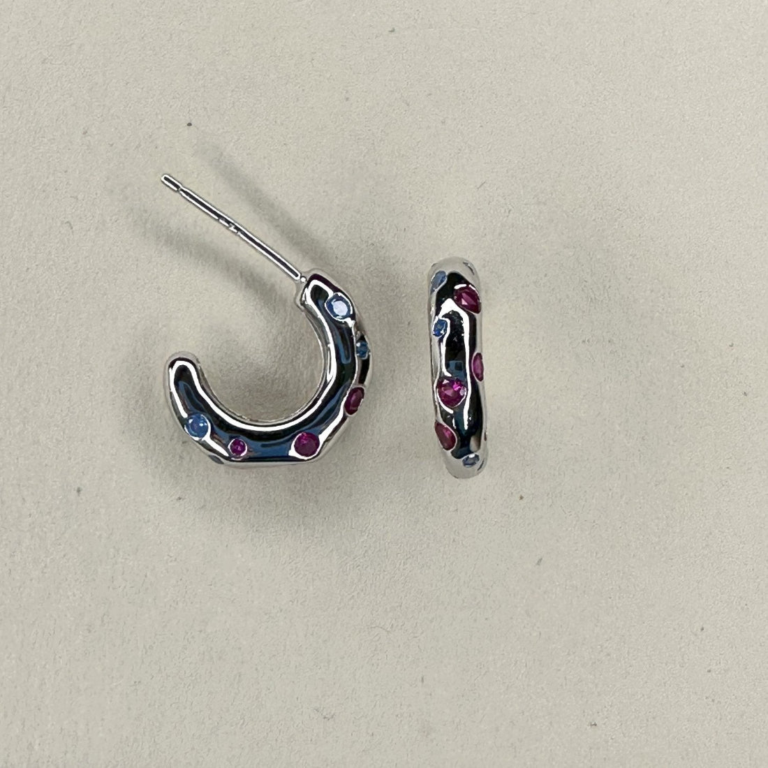 organic shape mini silver hoop earrings inlaid with different colour gemstones laid on cream ground