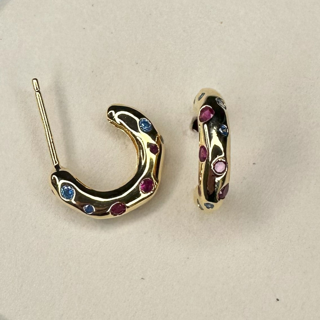 organic shape mini gold hoop earrings inlaid with different colour gemstones laid on cream ground