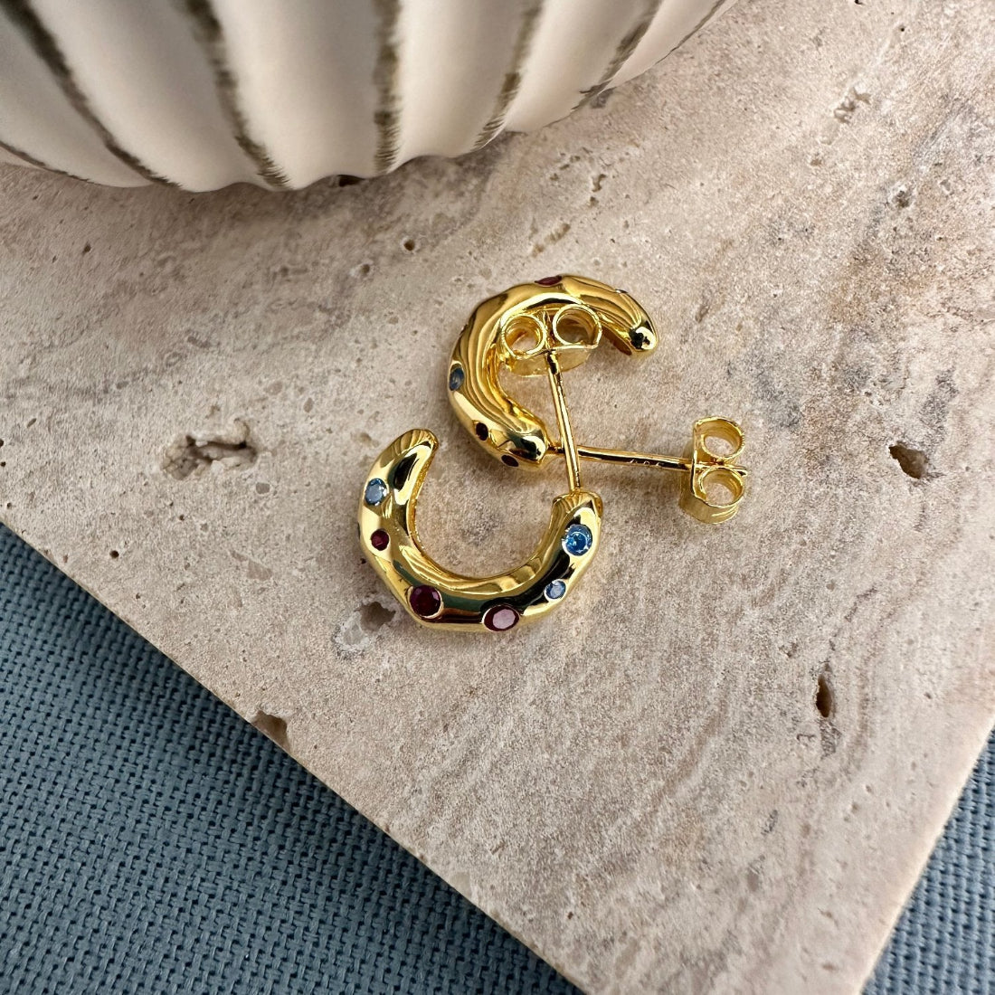 mini sized hoops in an organic shape set with multicoloured gemstones laid on a tile