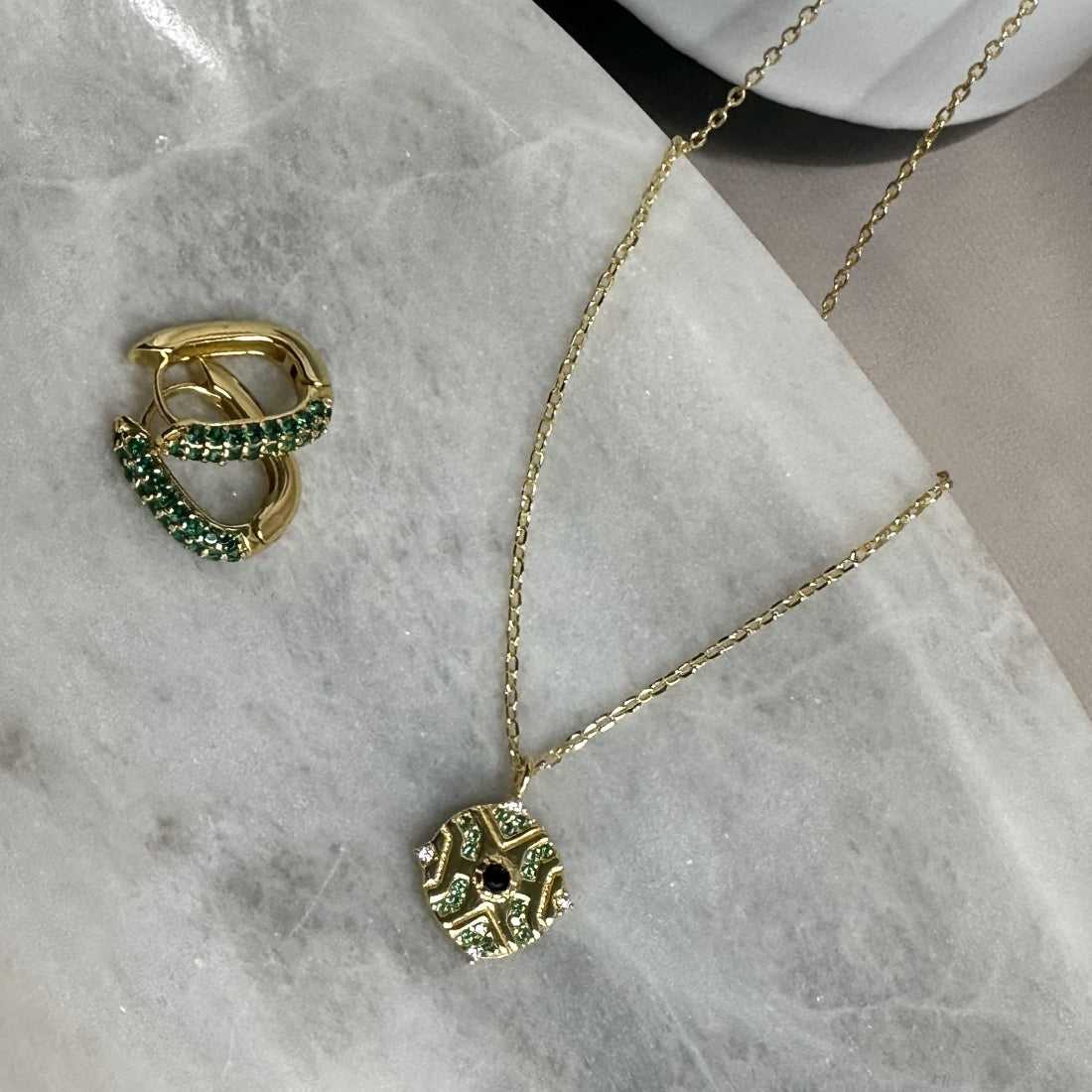 geometric moroccan inspired pendant along with a pair fo oval hoop earrings with emerald green crystal gemstones on a marble tray