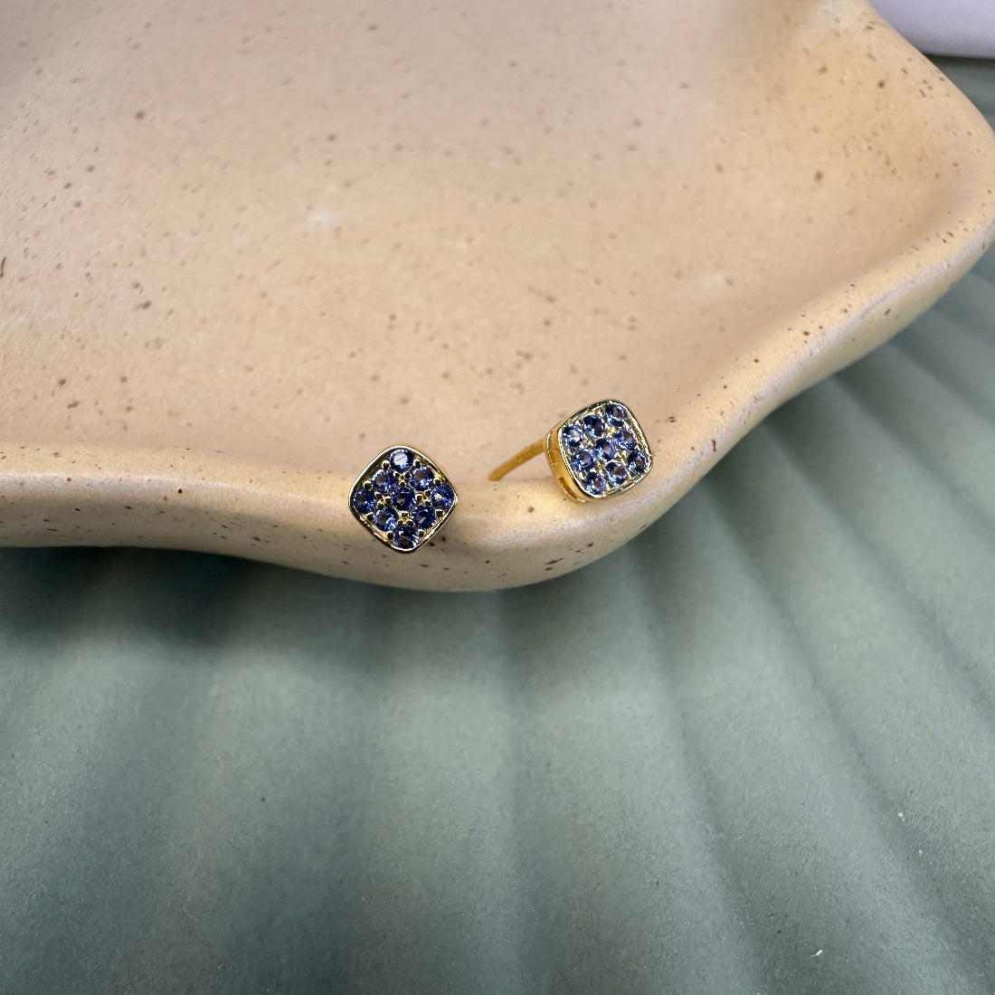 Pair of gold earrings with blue gemstones on a beige dish.
