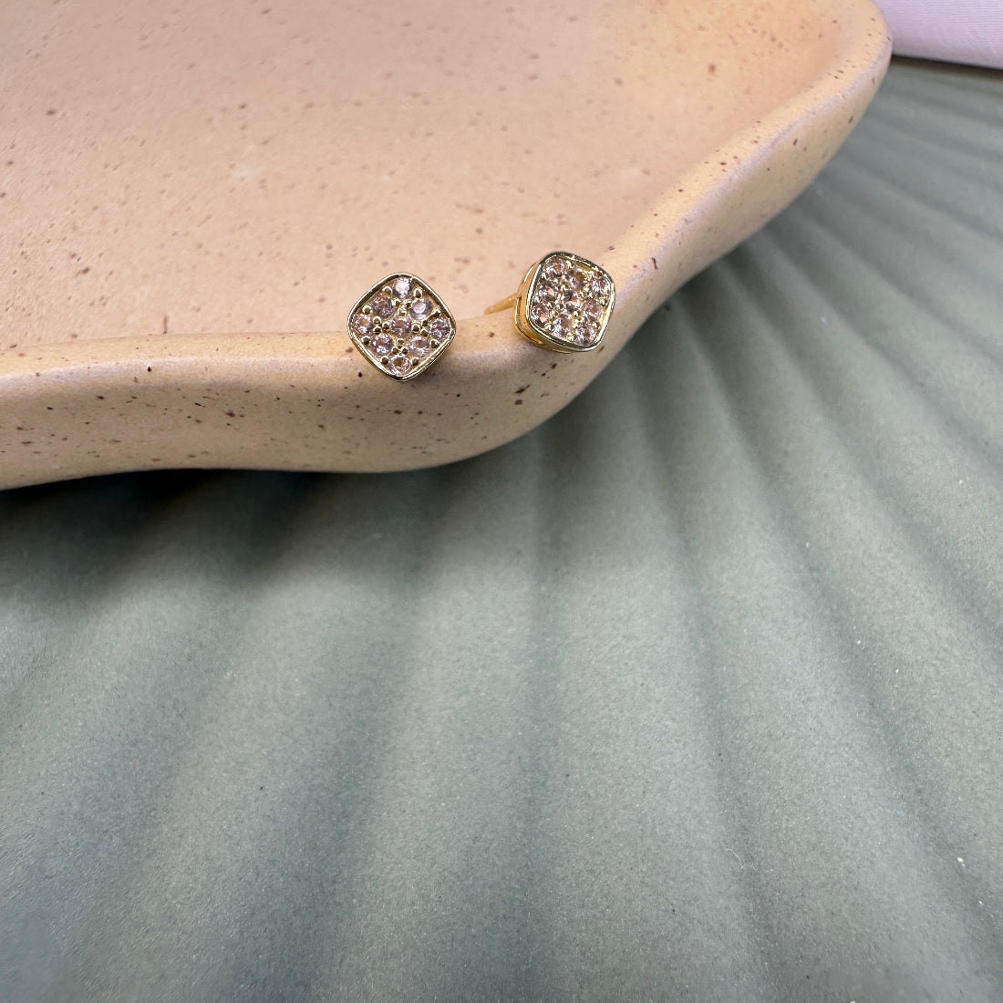 Pair of gold earrings with blushstones on a textured surface