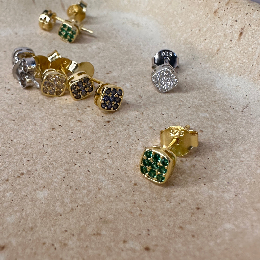 Gold and silver earrings with gemstones on a beige surface