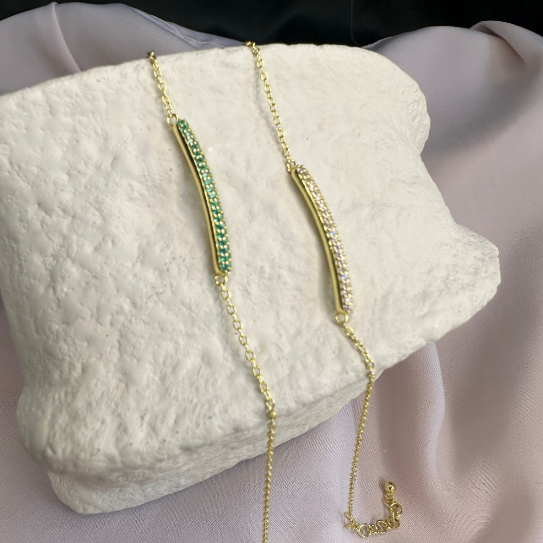 2 Gold bracelets with green and white stones on a textured white surface