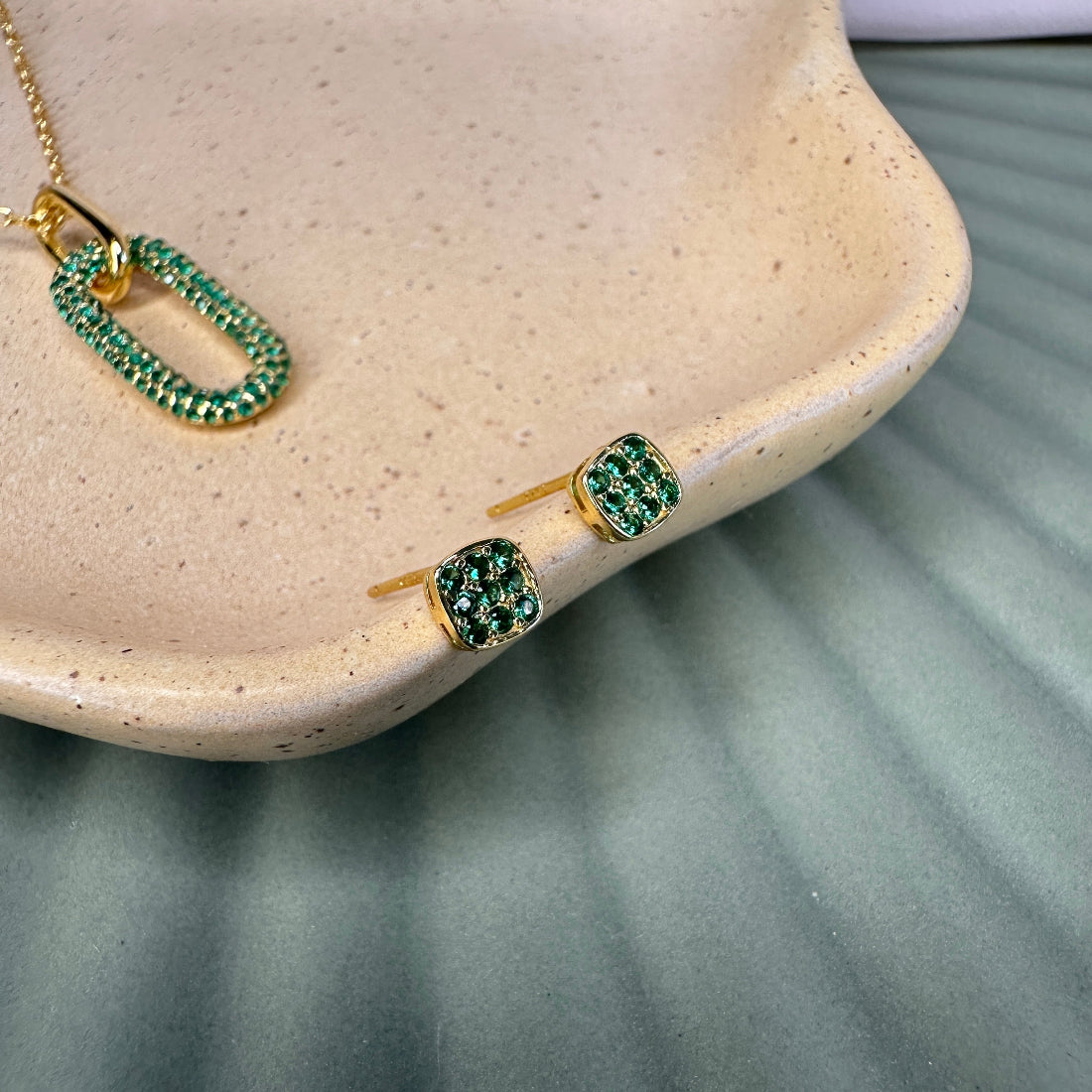 Gold jewelry set with green gemstones on a beige dish