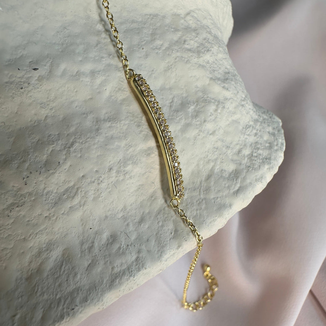 Gold bracelet with small crystal gemstones on a textured stone surface