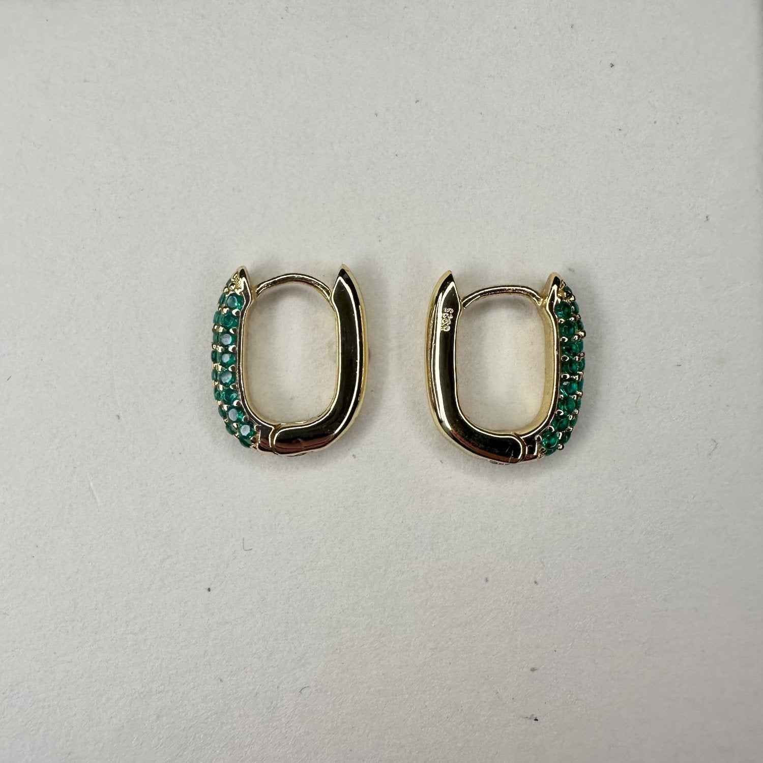 pave green gemstone gold hoops laid on a white matte plate