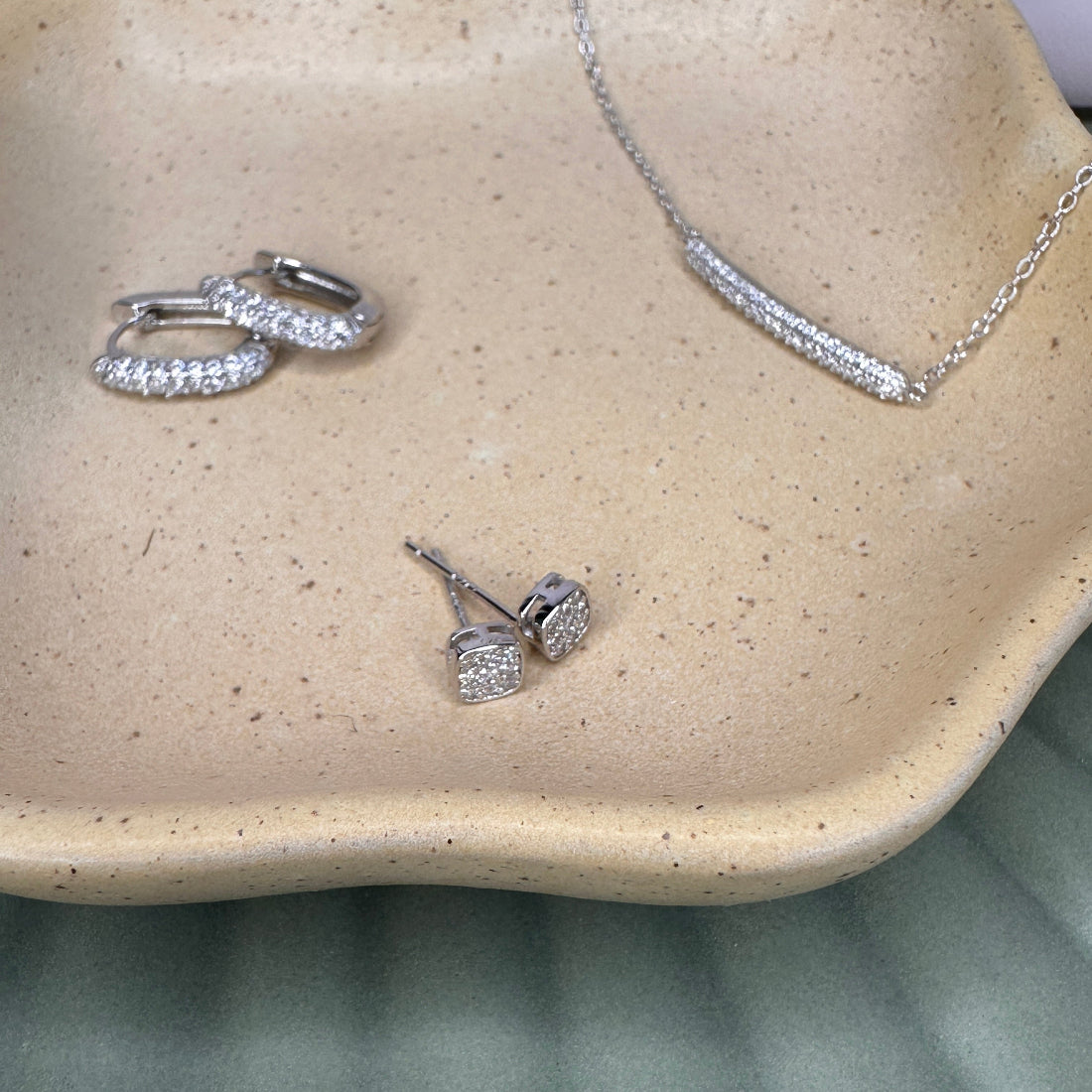 Silver jewelry set including earrings and a necklace on a beige dish.