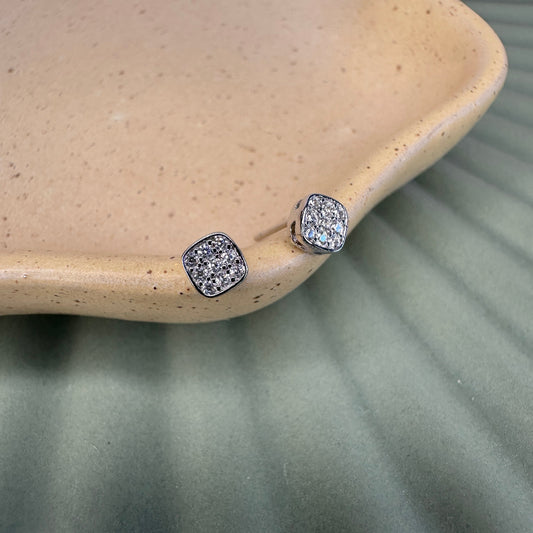 Pair of silver stud earrings on a textured beige surface