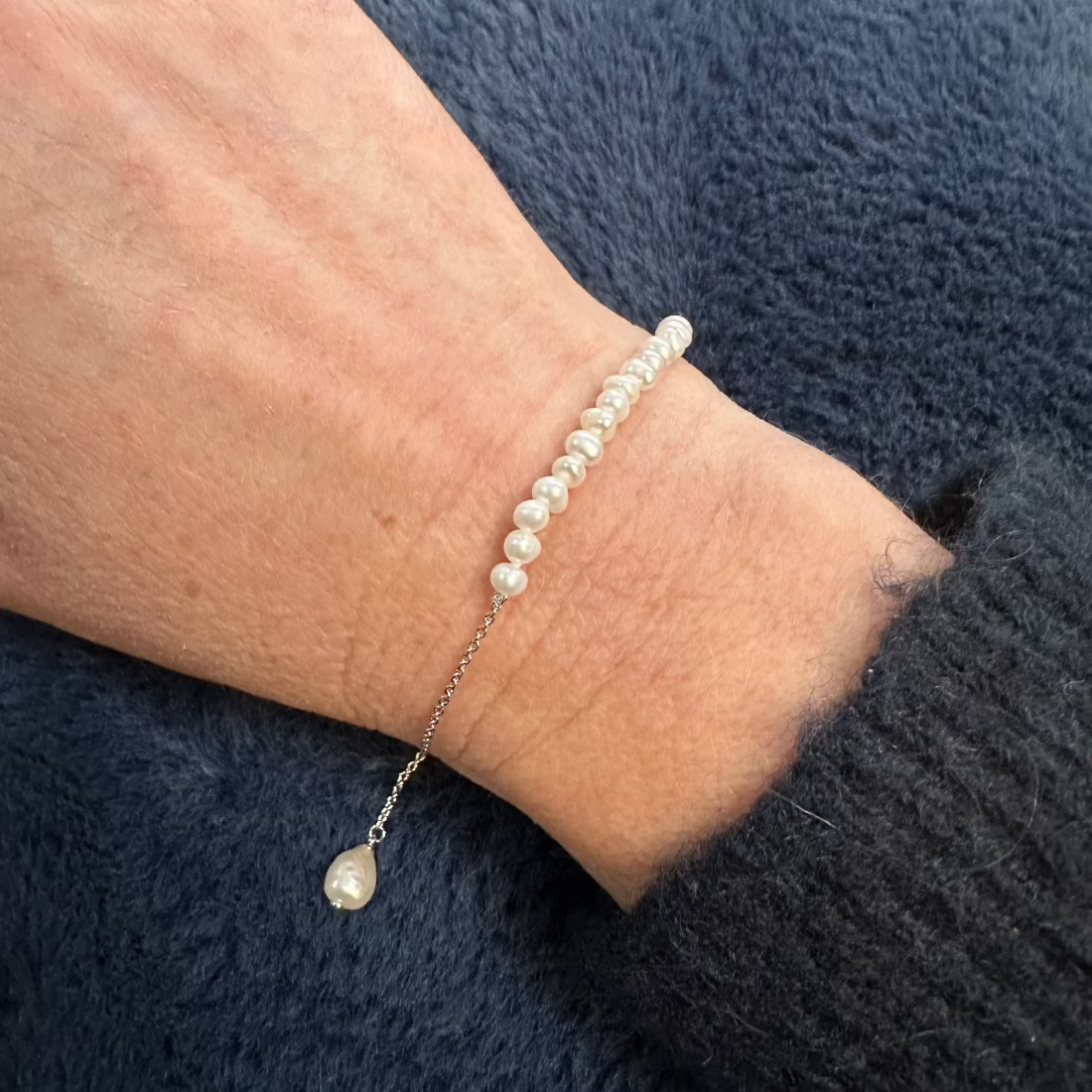 adjustable bracelet with freshwater pearl detail and pretty charm worn on model with blue jumper