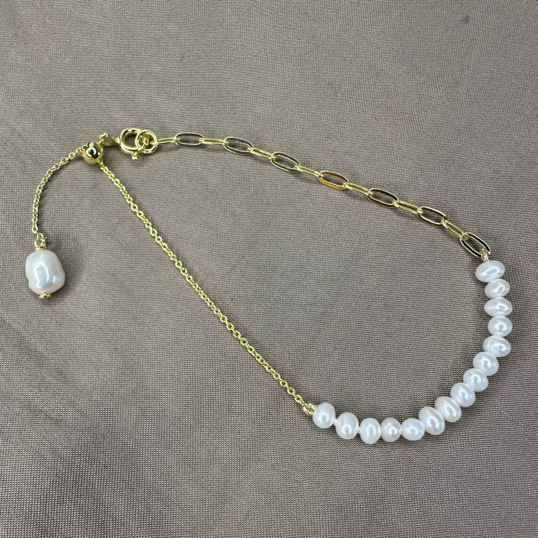 freshwater pearl bracelet with trending paperclip chain and adjustable extender with pearl charm.  Laid on brown ground