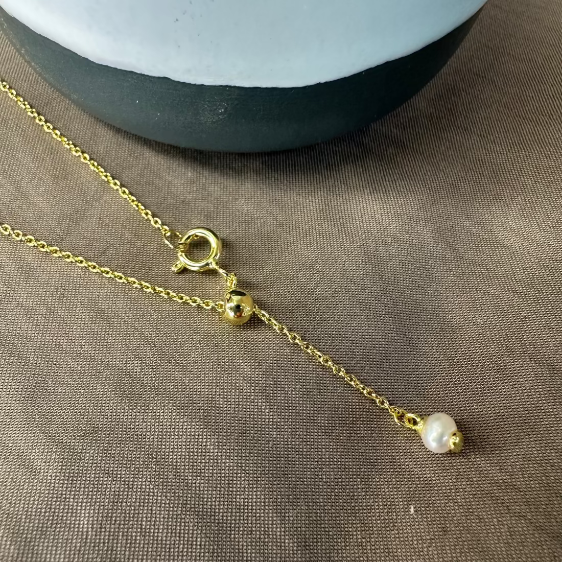 pearl charm on gold braclet laid on brown ground