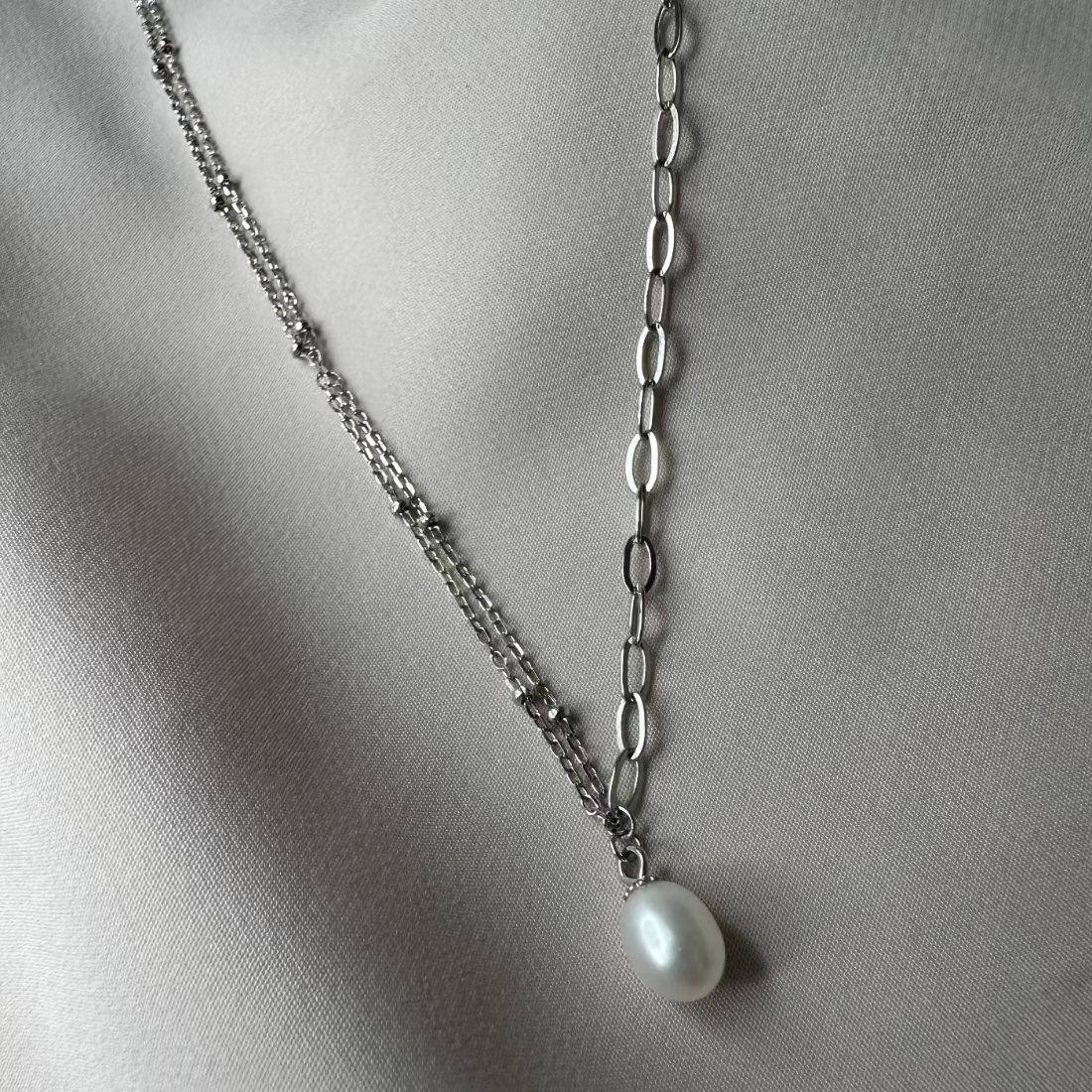 pearl charm necklace with double satellite chain on side and paperclip chain the other for a modern pearl look laid on cream ground
