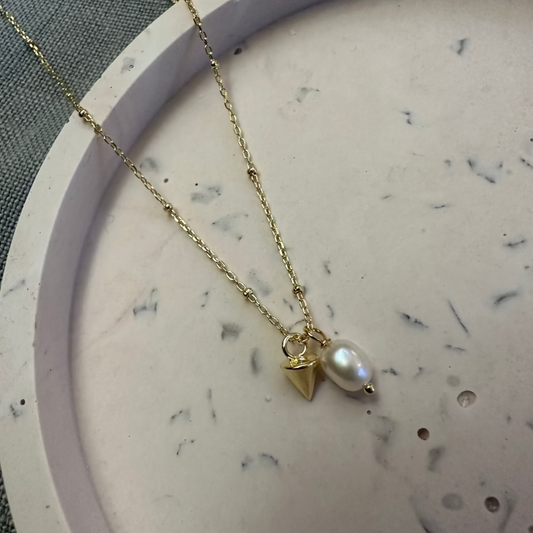 a charming pearl charm necklace with a gold cone charm laid on marble tray