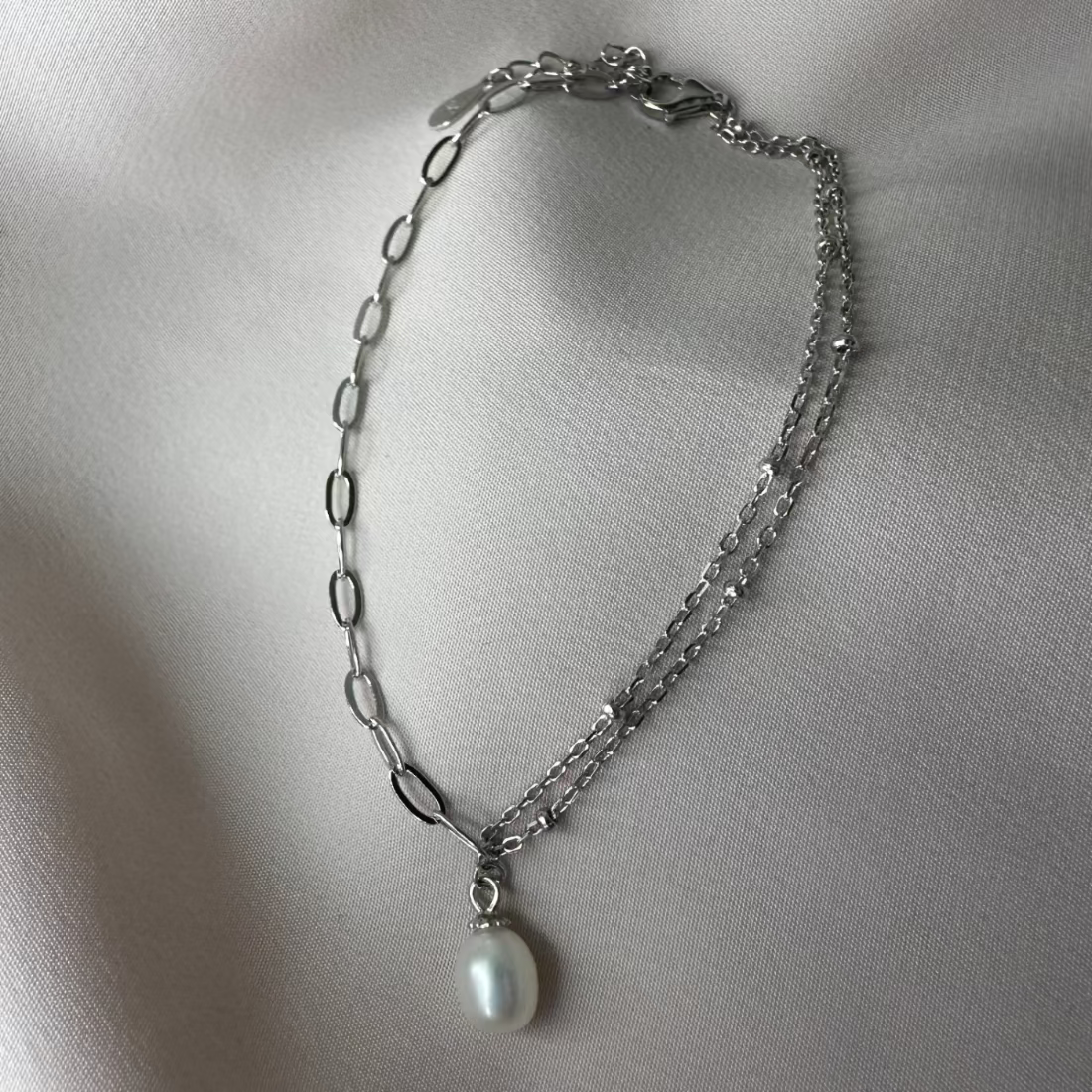 a freshwater pearl bracelet with trending paperclip chain and a contrasting double chain laid on a cream ground