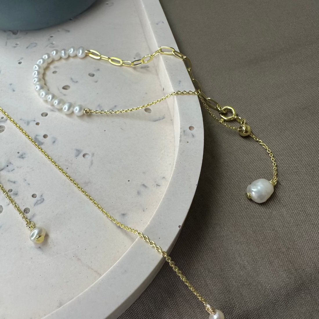 A bracelet with white freshwater pearls and an adjustable slider chain,  paperclip chain detail displayed on a marble surface.