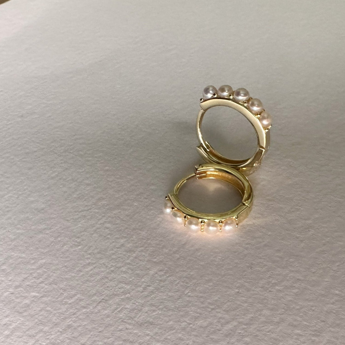 A pair of pearl hoop earrings with a gold band, featuring freshwater pearls.