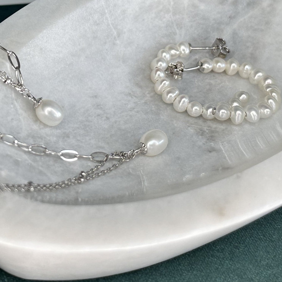 a collection of modern pearl jewellery in silver and freshwater pearls using modern chains and styles. laid on marble tray