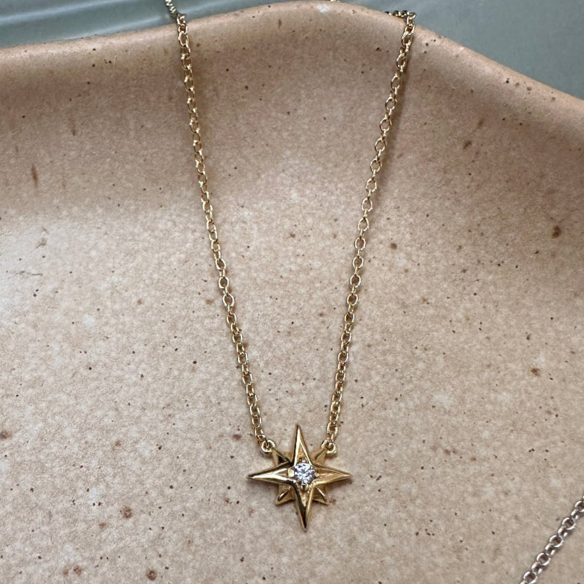 Gold star-shaped pendant necklace with gemstone on a textured beige surface