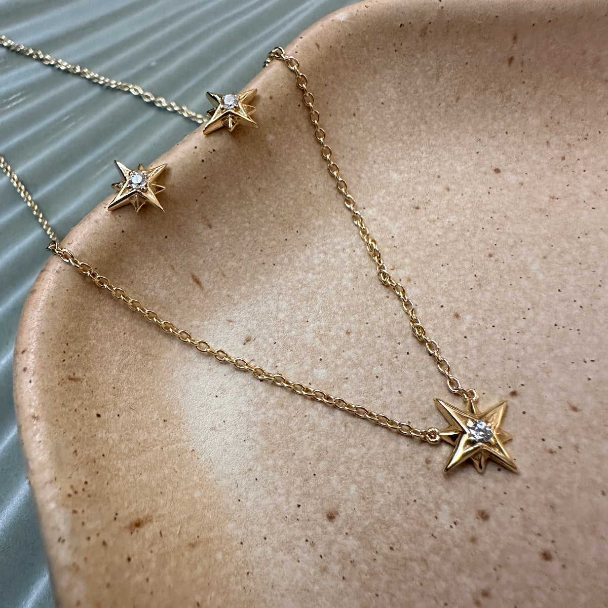 Gold star-shaped pendant necklace with matching star studs on a textured ceramic surface