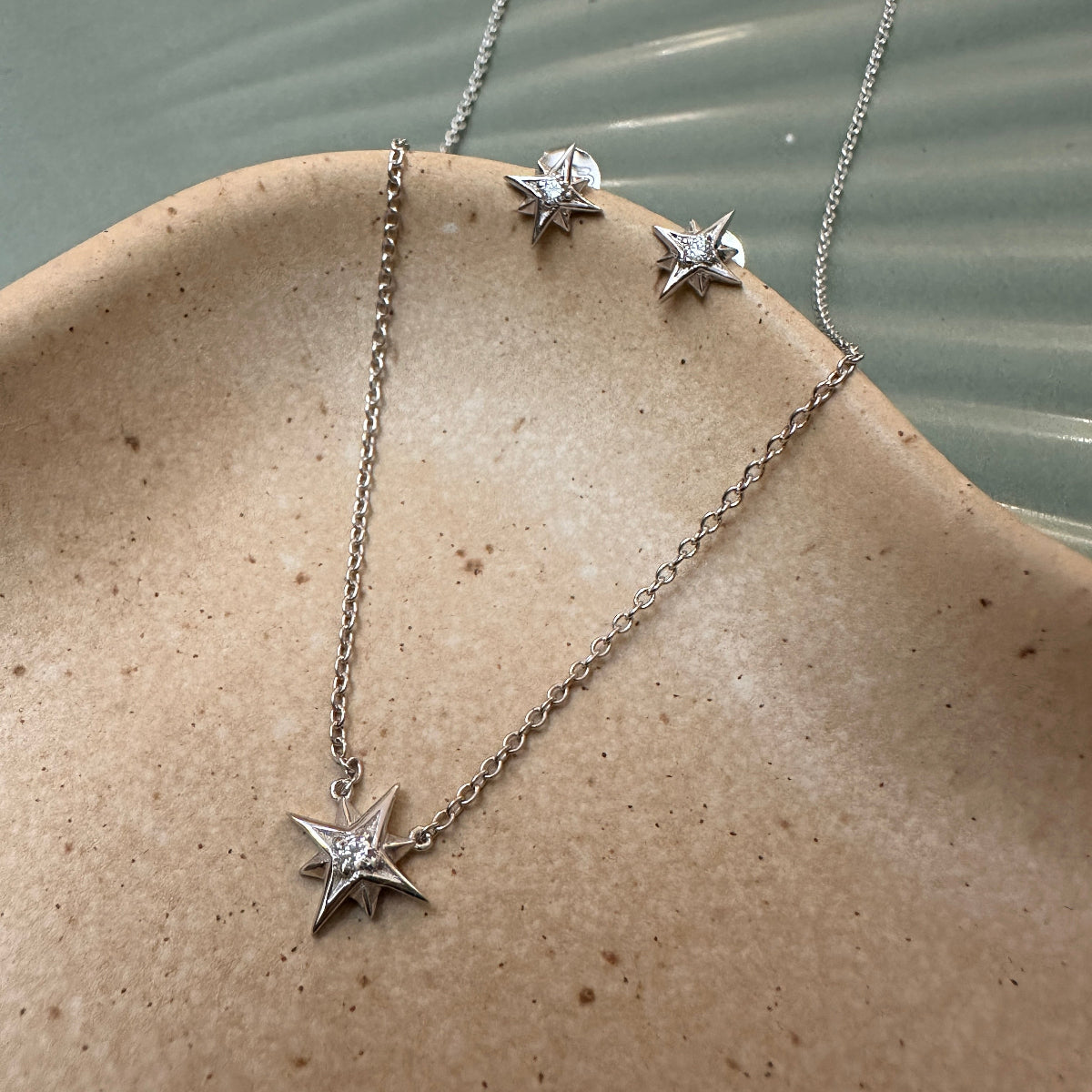 Star-shaped pendant silver necklace and matching earrings on a stone surface with water in the background