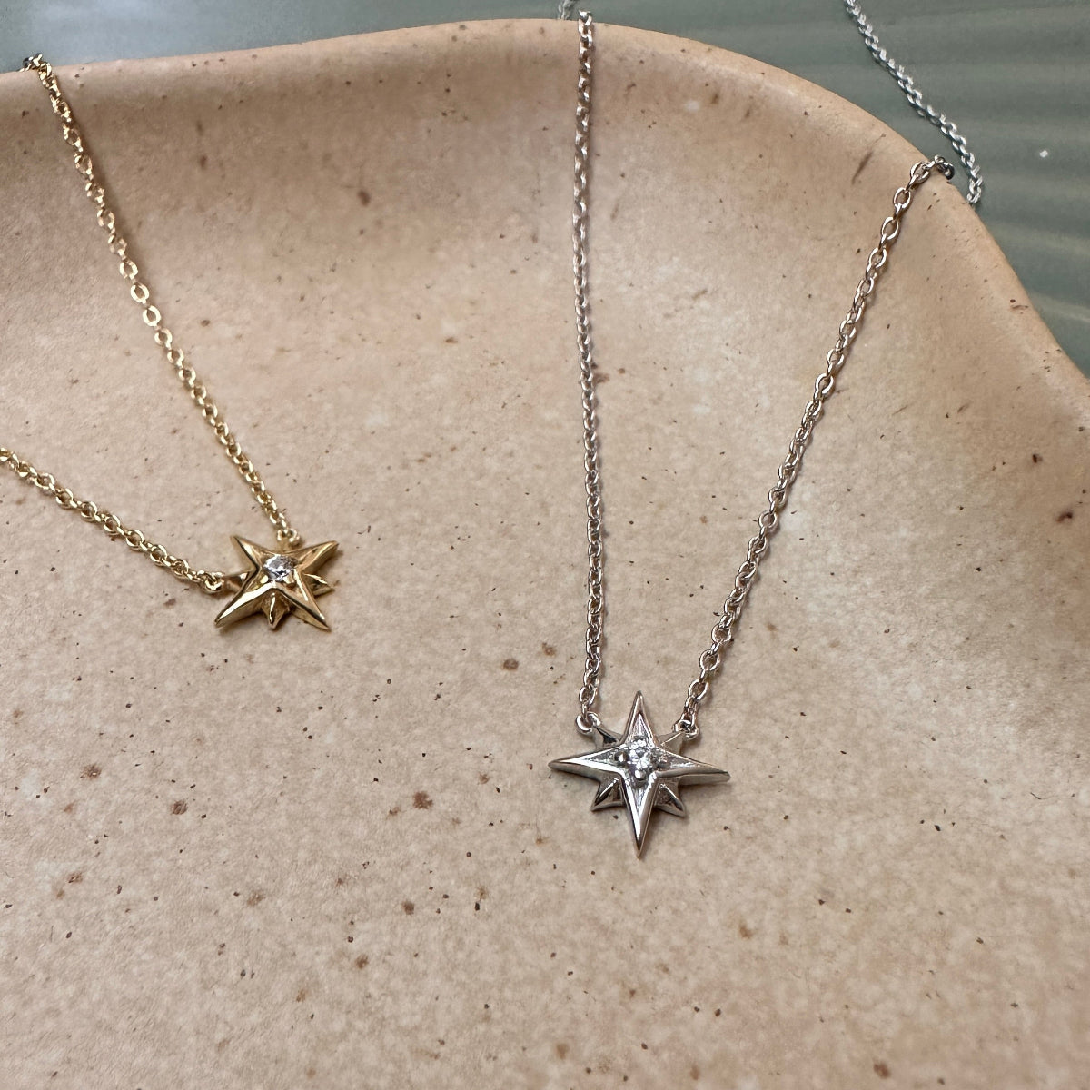 Two star-shaped pendant necklaces on a textured surface