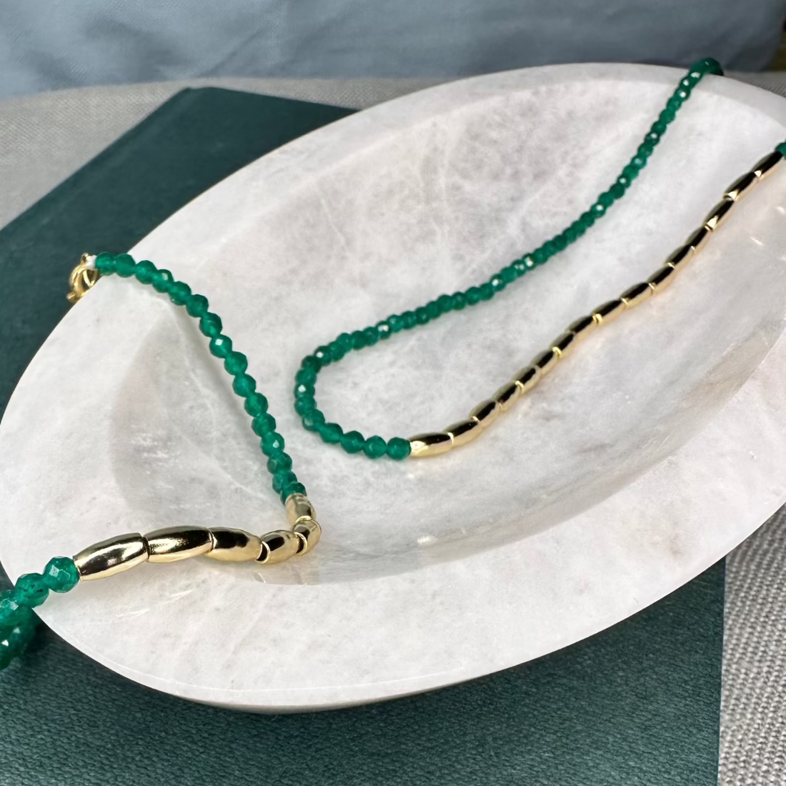 A gold nugget bracelet with green sparkling cubic zirconia beads ideal for layering displayed on a white surface.