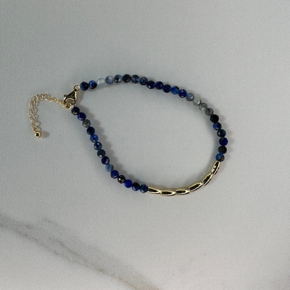 a gold nugget bracelet with blue  sparkling cubic zirconia beads ideal for layering displayed on a white ground