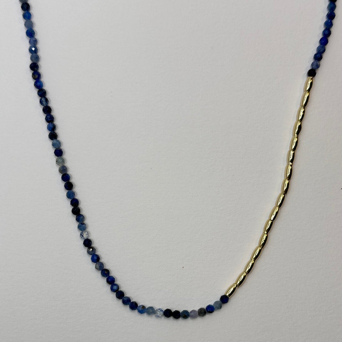 a gold nugget necklace with blue sparkling cubic zirconia beads ideal for layering displayed on a white ground