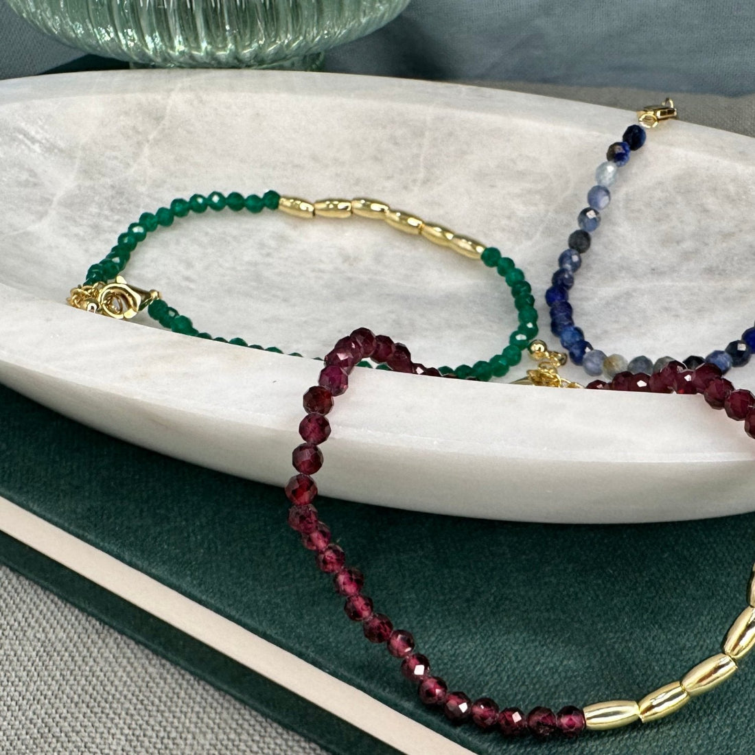 three gold nugget bracelets with green  red and blue sparkling cubic zirconia beads ideal for layering displayed on a marble tray